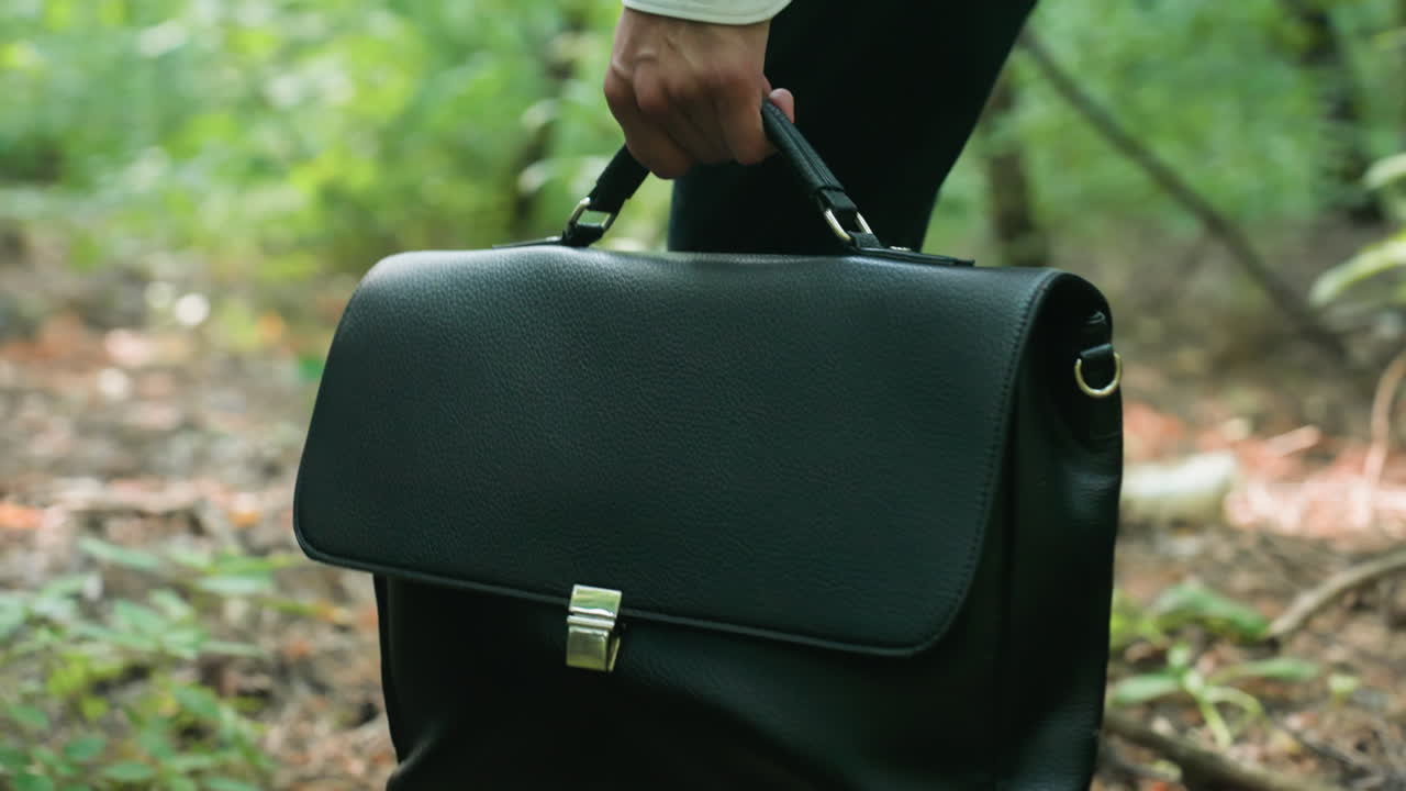Young biologist in white shirt and black trouser holding backpack while carefully moving through dense green forest under daylight, surrounded by trees, foliage, and wild vegetation