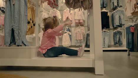 little child a girl sits in a clothing store under the windows dabbles and waits for her mother