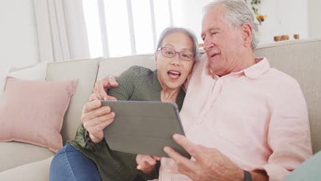 happy diverse senior couple using tablet and sitting on couch