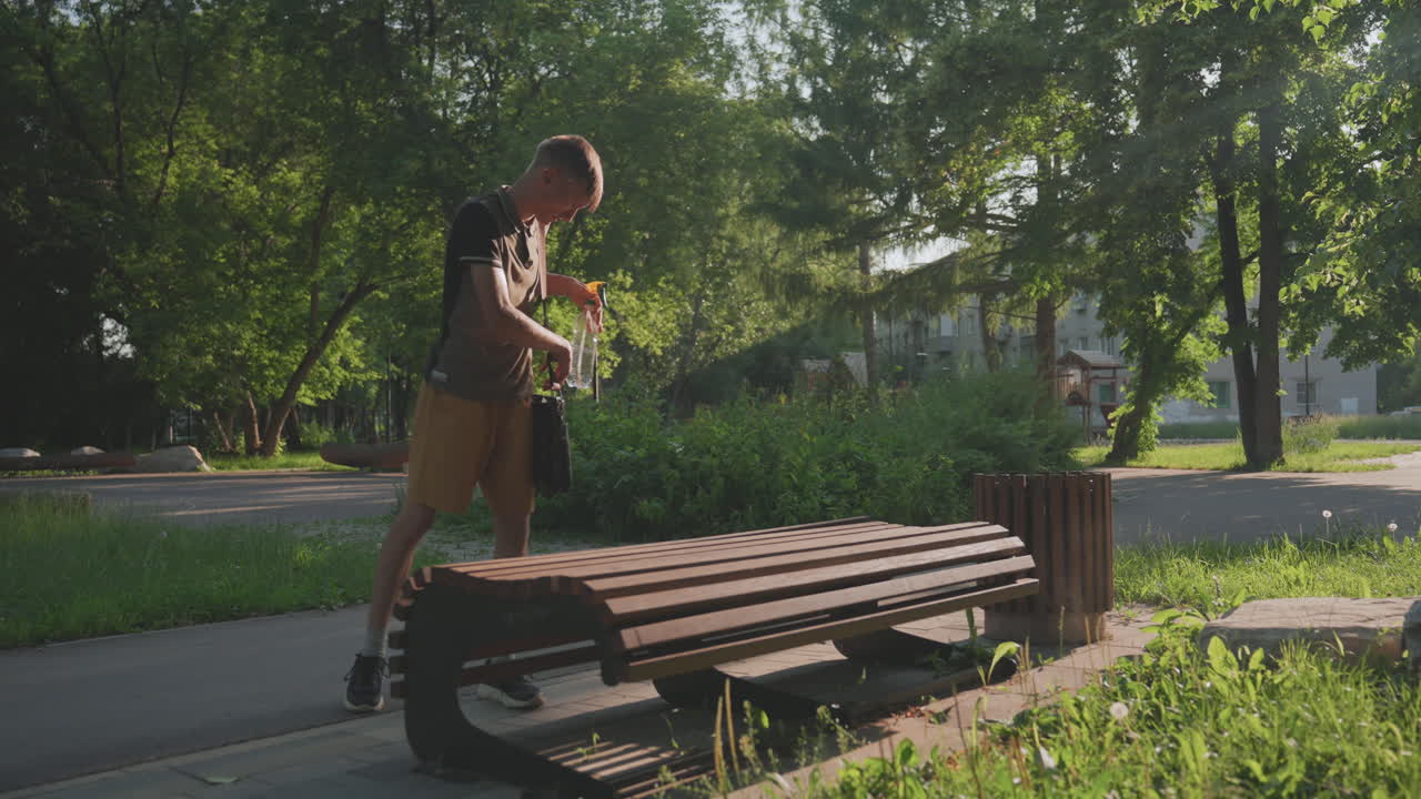 Person Disinfects Bench Carefully Outdoors, Man Maintains Sanitation On Park Furniture Diligently, Man Thoroughly Cleans And Disinfects Park Bench While Appearing Cautious And Attentive