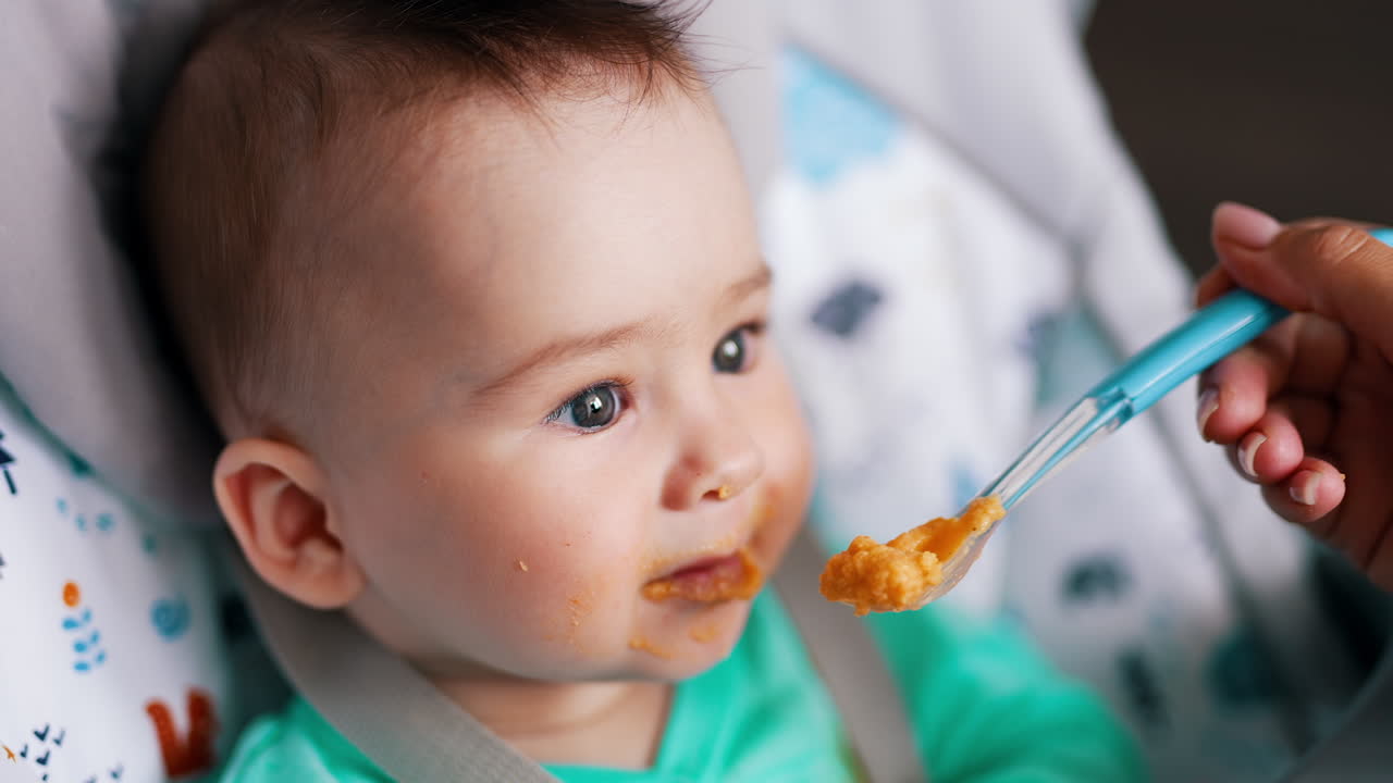 Mother is giving her son some food from a spoon. Nourishing babies concept. Close up. Blurred backdrop.