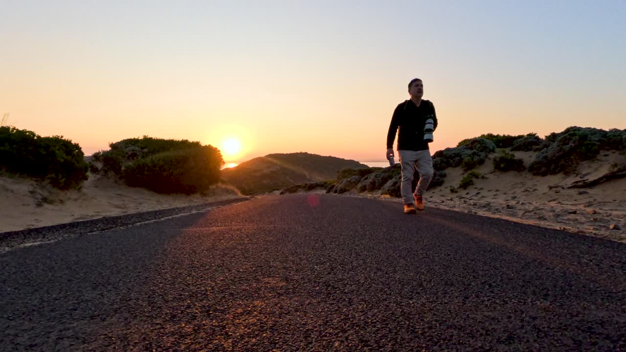 A person walks along a coastal road at sunset, capturing serene landscapes and warm lighting