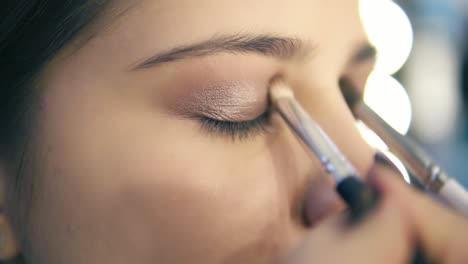 professional makeup artist using two makeup brushes to apply eye shadows. pro visagiste puts light brown shadows on eyelid of a