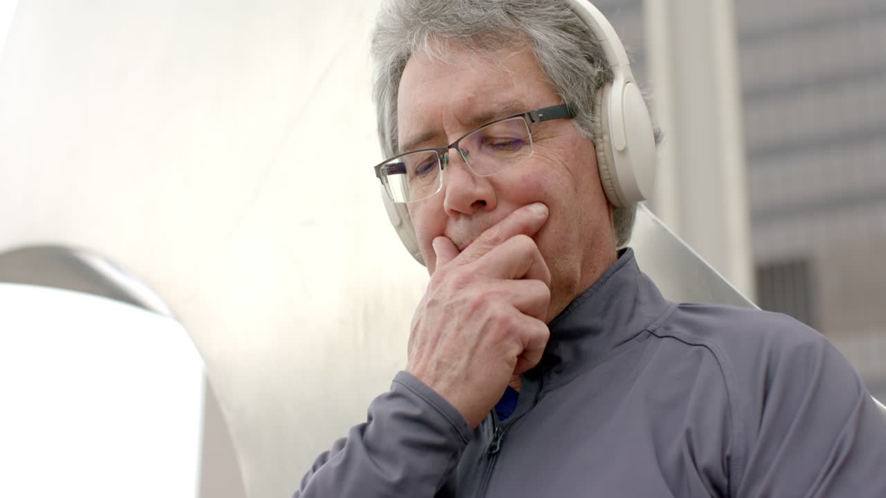 Senior man tapping and swiping rugged smartphone while unzipping jacket and leaning in lounge area