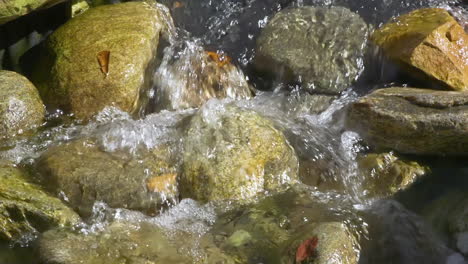 Close-view-of-rounded-stones-and-rocks-in-a-small,-quickly-flowing-stream-of-fresh,-clear-water