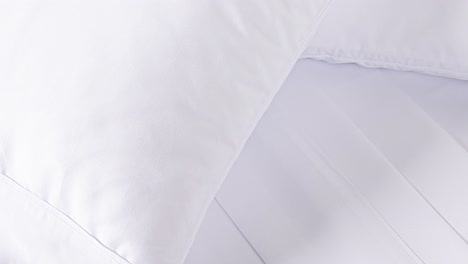 white linens and pillows pan slowly across bed in soft light