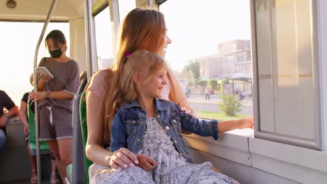 family rides in public transport, mother with little daughter sit together and look out window tram