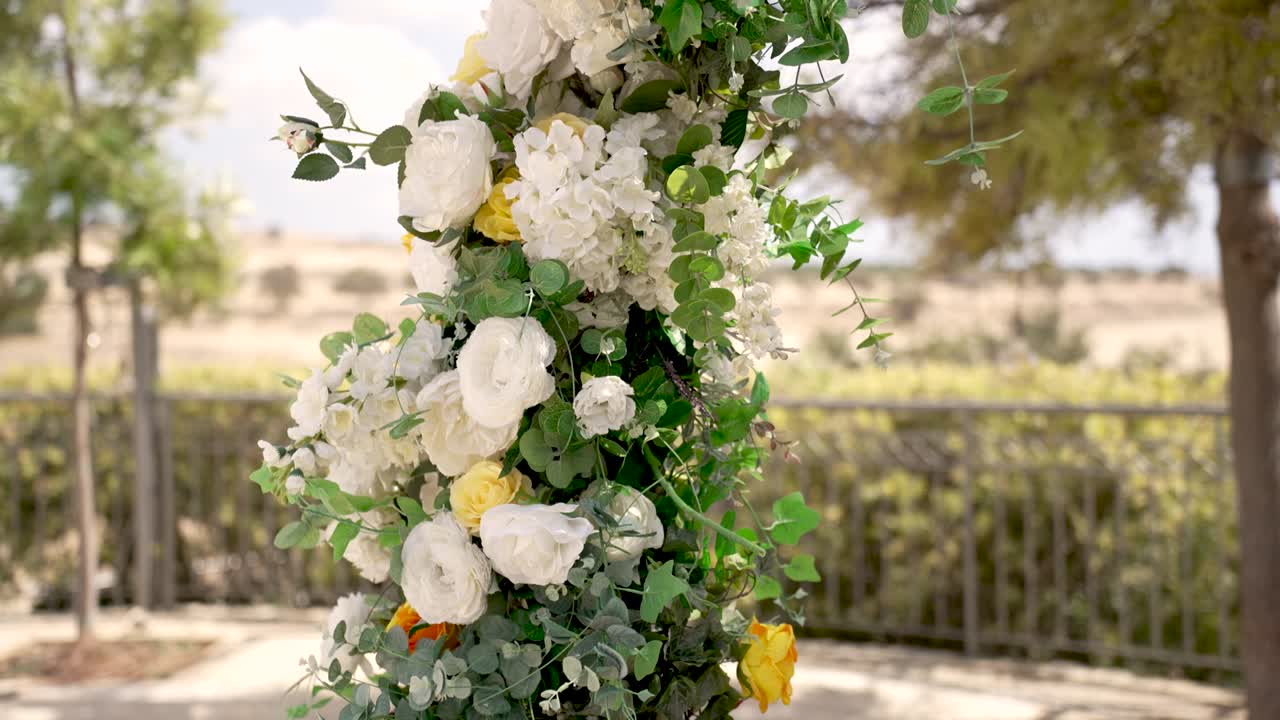 En fantastisk utstilling av hvite og gule blomster skaper et elegant blomsterarrangement i en utendørs hage. Denne settingen er perfekt for et bryllup eller en spesiell begivenhet, omgitt av grøntområder.
