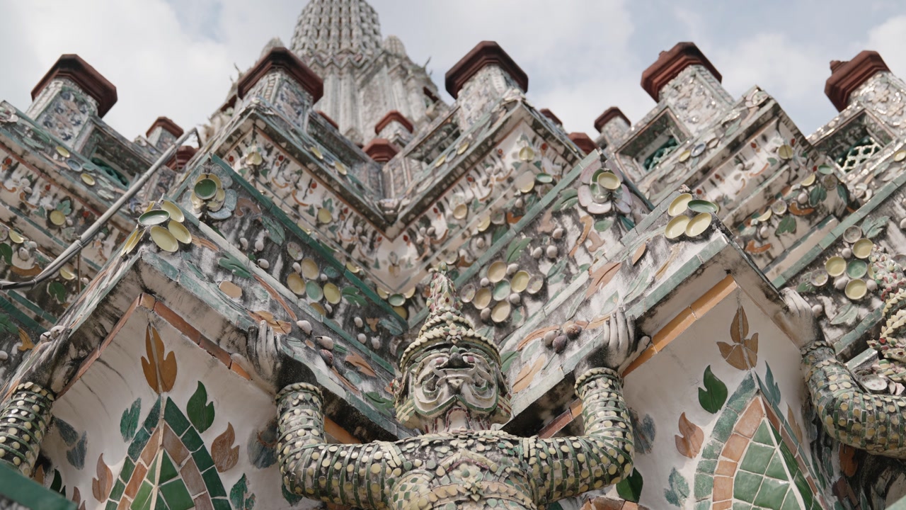 An intricate temple facade at Wat Arun in Bangkok, Thailand, featuring detailed guardian statues decorated with colorful mosaic tiles