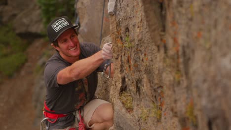 a rock climber attaches a carabiner as he scales a rock wall