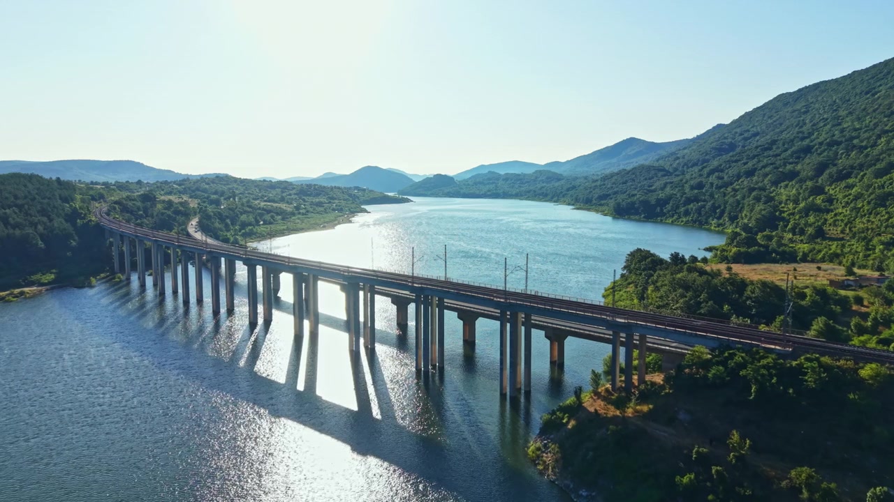 昼間、水上を渡る橋と鉄道の交差点の眺め、背景には山々