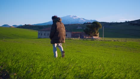 a man walks toward mount etna with a clear view of the active volcano during winter sunrise in sicily