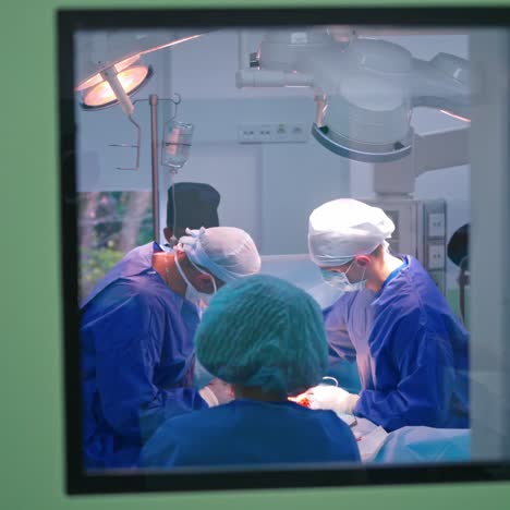 modern operating theatre. teamwork of surgeons in medical uniform perform an operation to a patient in surgery room. view through the window.