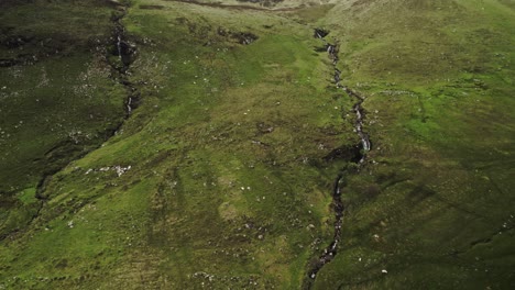 Sheep-Graze-As-Gentle-Waterfalls-Cascade-Down-Scottish-Highland-Cliffside,-Skye