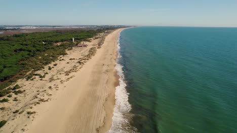 establishing aerial view over huelva spanish golden sandy woodland beach and coastal lighthouse tower in the distance