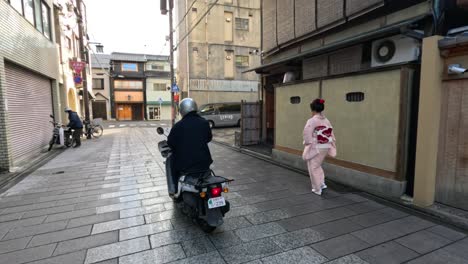 person in kimono walks as motorcyclist passes by.