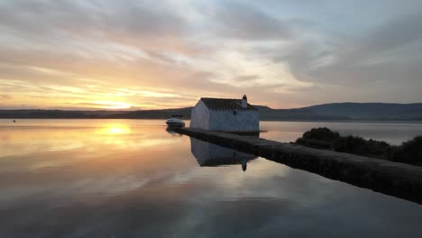 Lake-house-with-boat-parked-in-front-sitting-on-the-waters-edge-with-sunset-reflecting-off-water