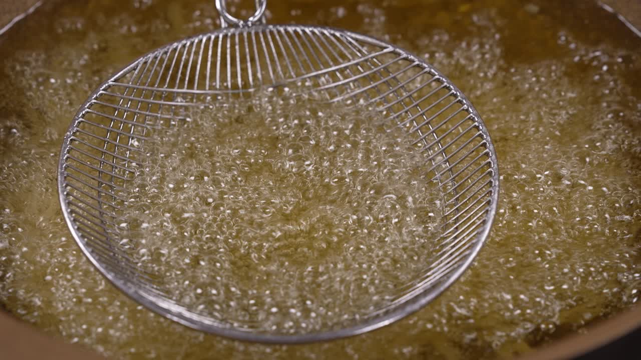 Olio caldo in padella pronto per la frittura di cibi con schiumarola e utensili da cucina, primo piano della cottura.