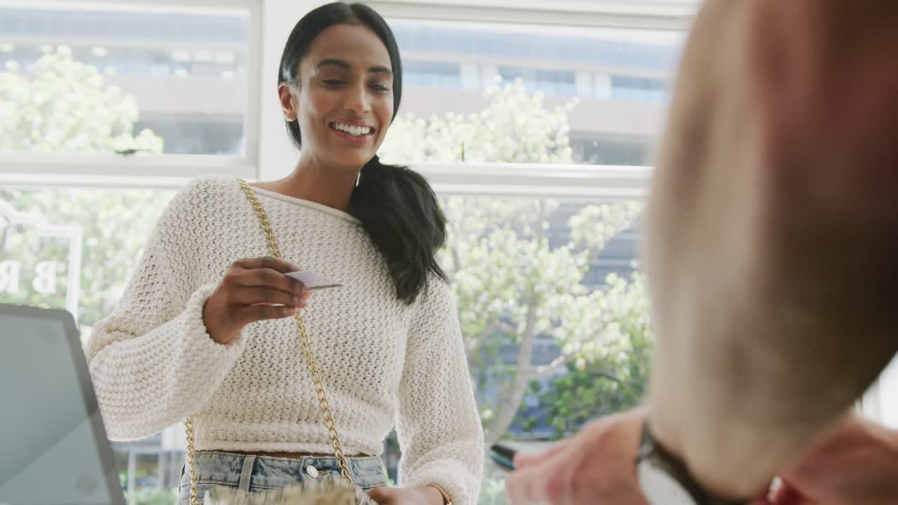 Happy biracial woman paying with credit card in cafe