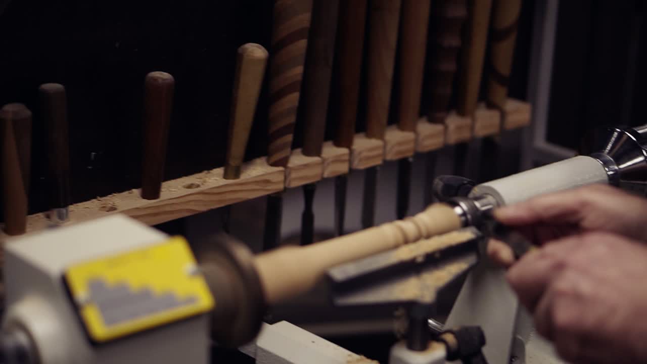 From the variety of tools man choosing the right size planer. Carpenter male hands cutting wooden knob out of wood piece spinning on machine using chisel, working on the form, decoration. Slow motion