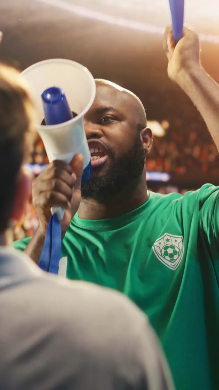Vertical video Man chants through megaphone in football stadium stands