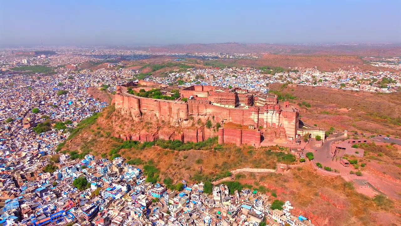 Un'ampia inquadratura statica dall'alto dello storico Forte Mehrangarh che si erge sopra le iconiche case dipinte di blu della città di Jodhpur, sotto un cielo luminoso, Rajasthan, India