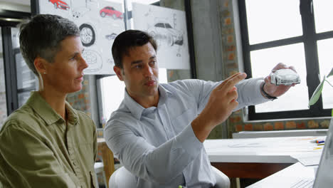 Car-designers-discussing-over-model-car-at-desk-4k