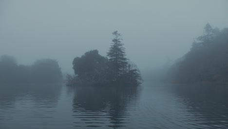 atmospheric tracking towards tree covered island surrounded with fog