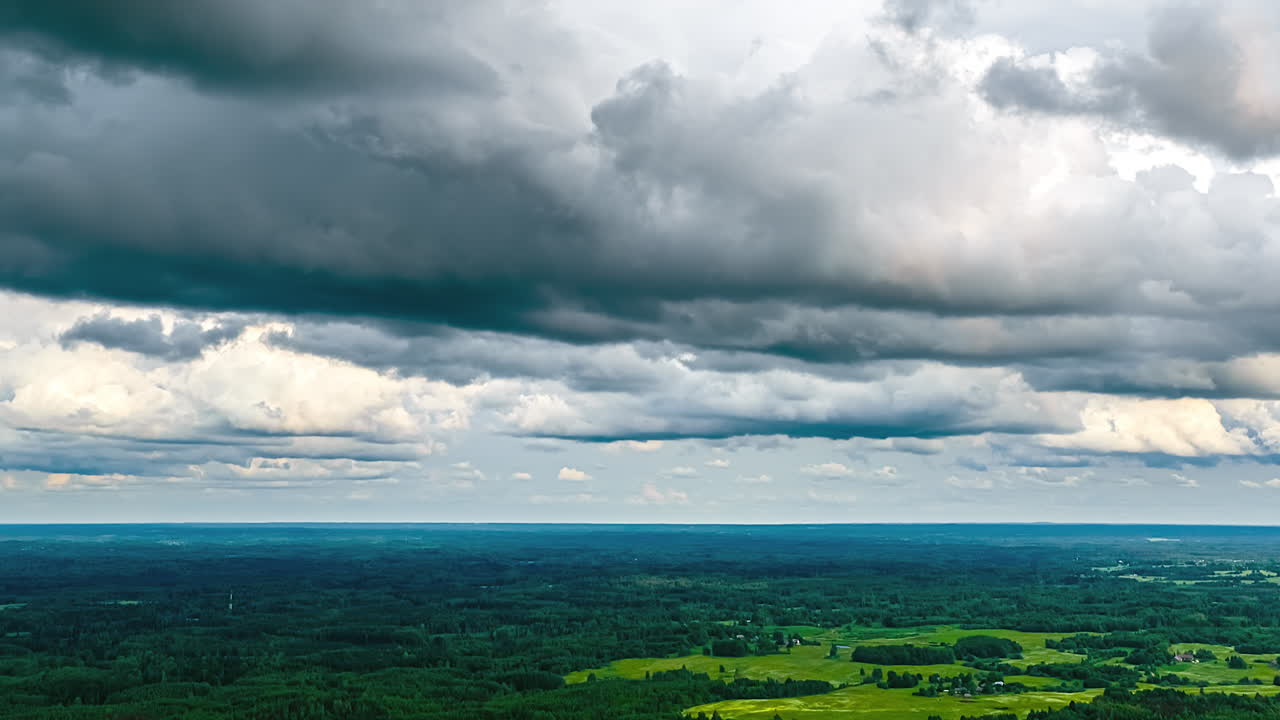 Aerial time-lapse of dramatic storm clouds and shadows moving quickly over a vast and vibrant green forest landscape, creating a moody and epic nature scene