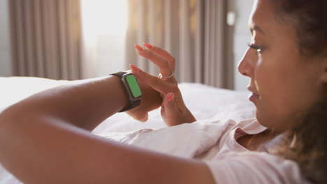 Mujer-Sentada-En-La-Cama-Mirando-La-Pantalla-Del-Reloj-Inteligente