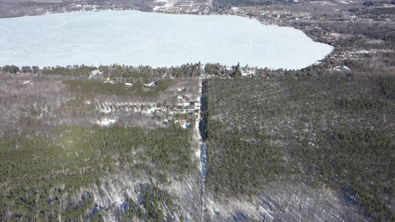 Letecký pohled sledující mezinárodní hranici oddělující Quebec, Kanadu a Vermont, Spojené státy, se zamrzlým jezerem a sněhem pokrytými stálezelenými lesy viditelnými za slunečného zimního dne
