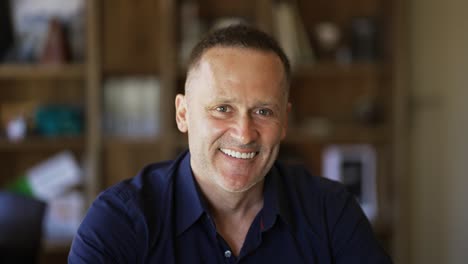 An-adult-man-with-stubble-in-a-black-shirt-sitts-in-a-cafe-smiling-and-posing-for-the-camera