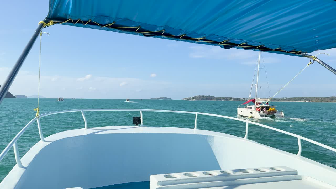 A boat sails through turquoise waters under clear skies in Chalong Bay, Phuket, capturing serene ocean views and distant islands