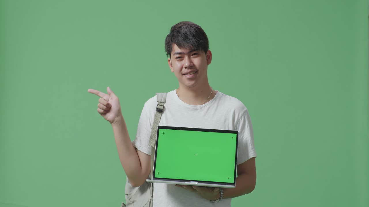 아시아 남성 학생이 노트북 모형을 보여주고 녹색 화면에 손가락을 직접 으로 표시합니다.