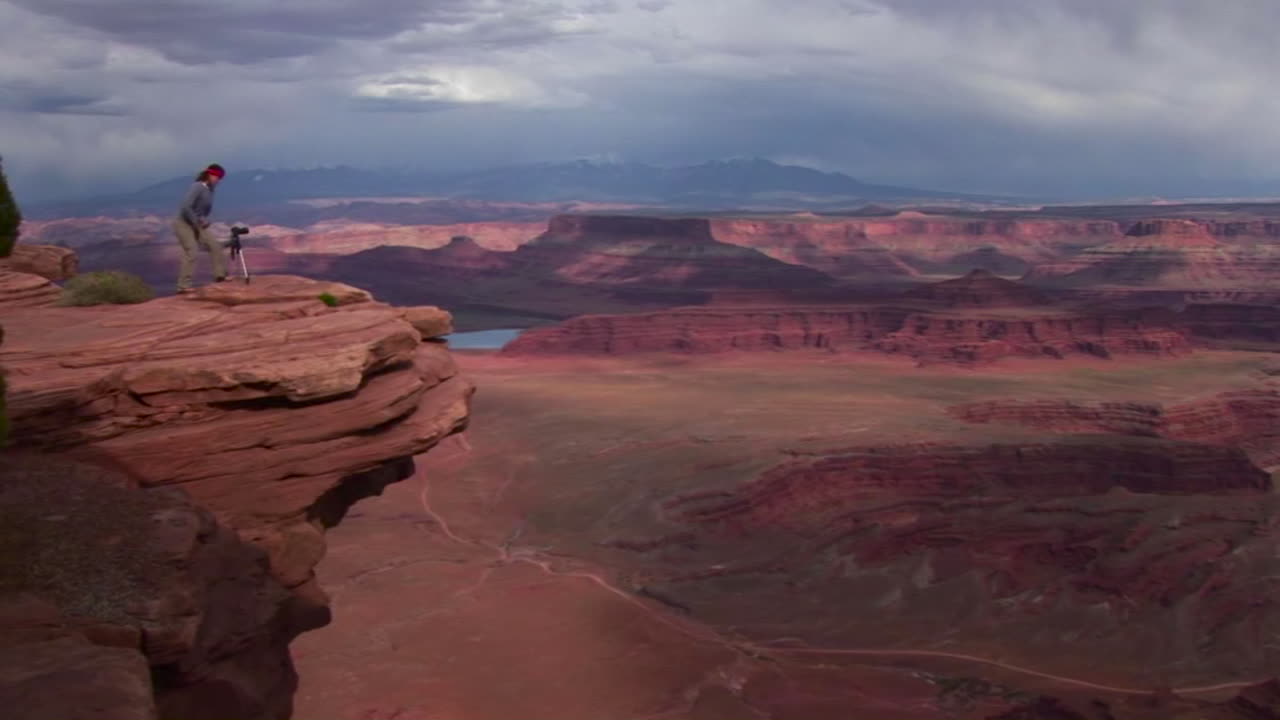 фотограф идет к уступу, с которого открывается вид на долину мез днем в национальном парке каньонлендс в штате юта