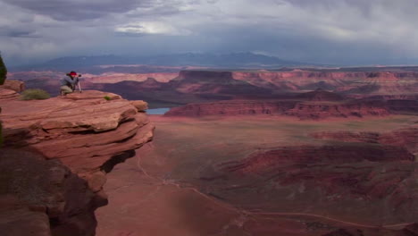 A-photographer-walks-to-a-ledge-that-overlooks-a-valley-of-mesas-at-day-in-Canyonlands-National-Park-in-Utah