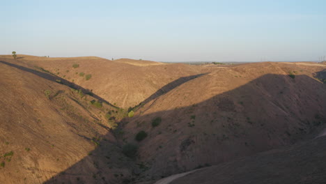 Tilt-down-reveal-shot-of-valley-between-Rolling-Hills-at-golden-hour-in-Algarve,-Portugal