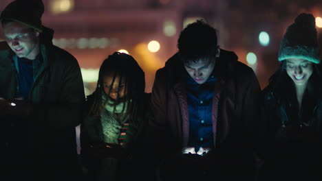 group of friends using smartphone mobile technology hanging out on rooftop at night enjoying weekend sharing social media messages