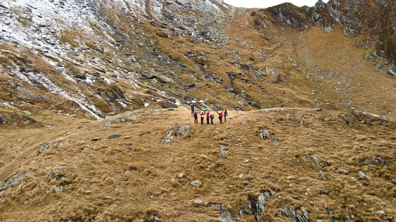 Vista aerea con drone della natura in Romania. Strada Transfăgărășan sui monti Carpazi, gruppo di turisti che scattano foto vicino a pendii rocciosi coperti di neve