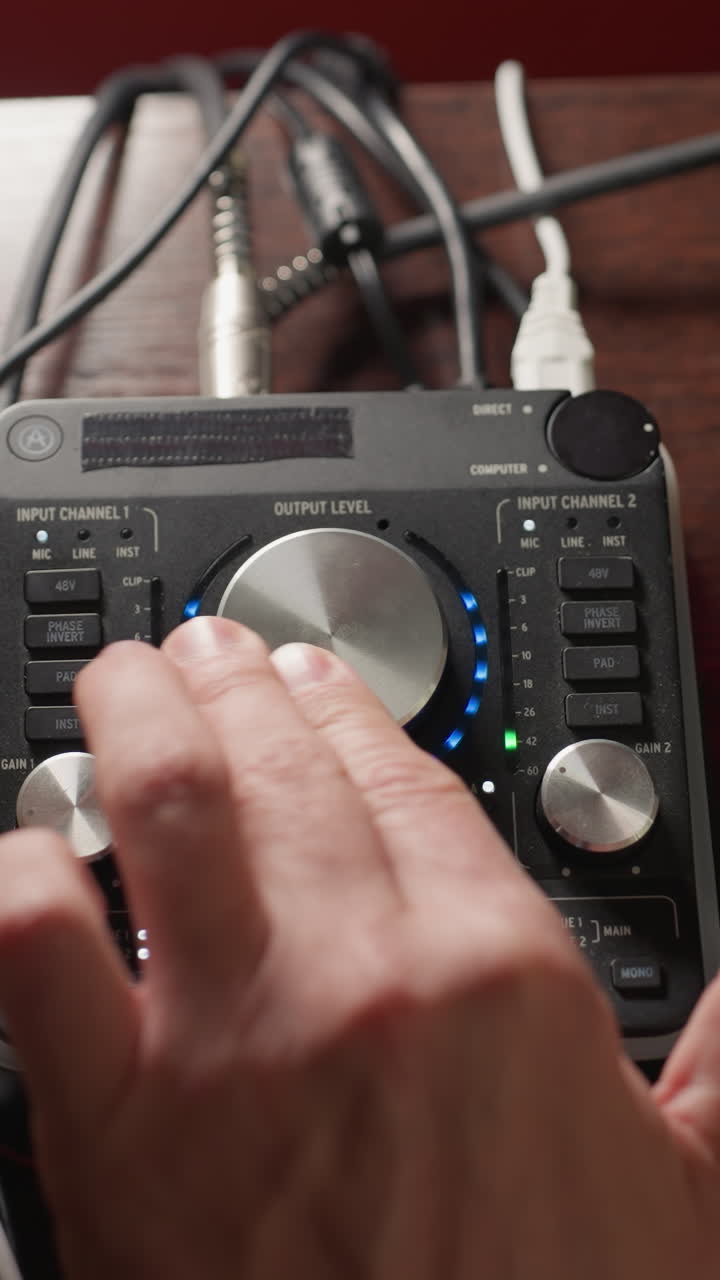 소리 서 (sound mixer) 를 작동하는 손의 클로즈업, 오디오 레벨을 조정하기 위해 손잡이를 회전시키는 것. 소리 엔지니어링에 관여하는 정확한 작업, 다양한 케이블이 서에 연결되어 있습니다.