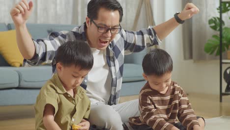 close up of asian father and sons assemble the construction set colorful plastic toy brick on a mat at home