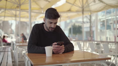 man using mobile phone in outdoor cafe