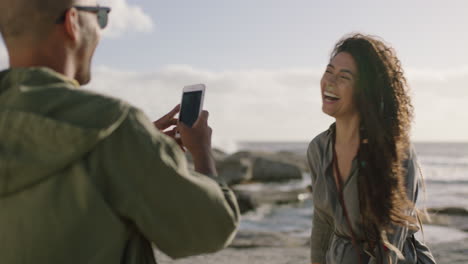 feliz pareja de raza mixta tomando fotos en la playa usando el teléfono mujer posando un signo de paz