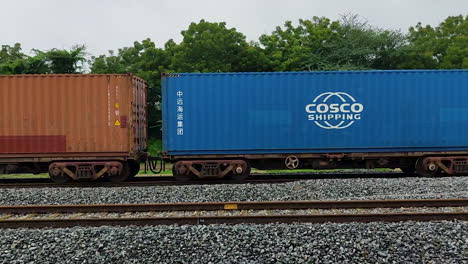 passenger train speeds past stationary freight train, highlighting vibrant contrast and interaction between different types of rail transport.