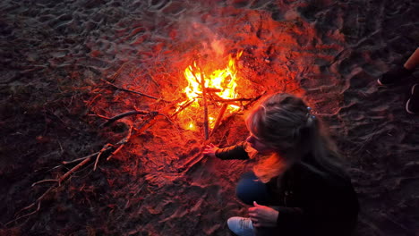 mujer rubia blanca en la playa está cuidando del fuego en la arena, cámara lenta