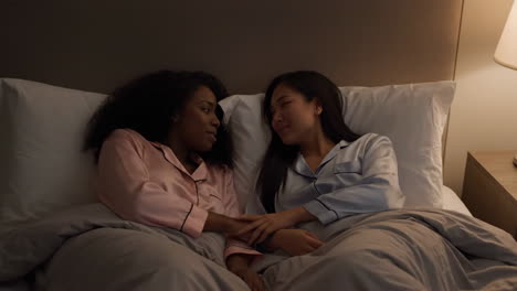 two women in pajamas conversing in bed