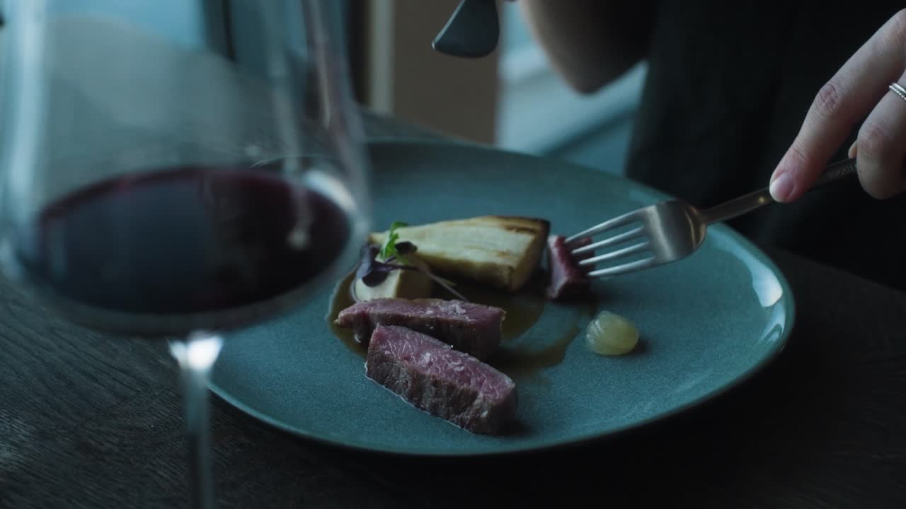 Person cutting into steak slices on fine dining plate in restaurant