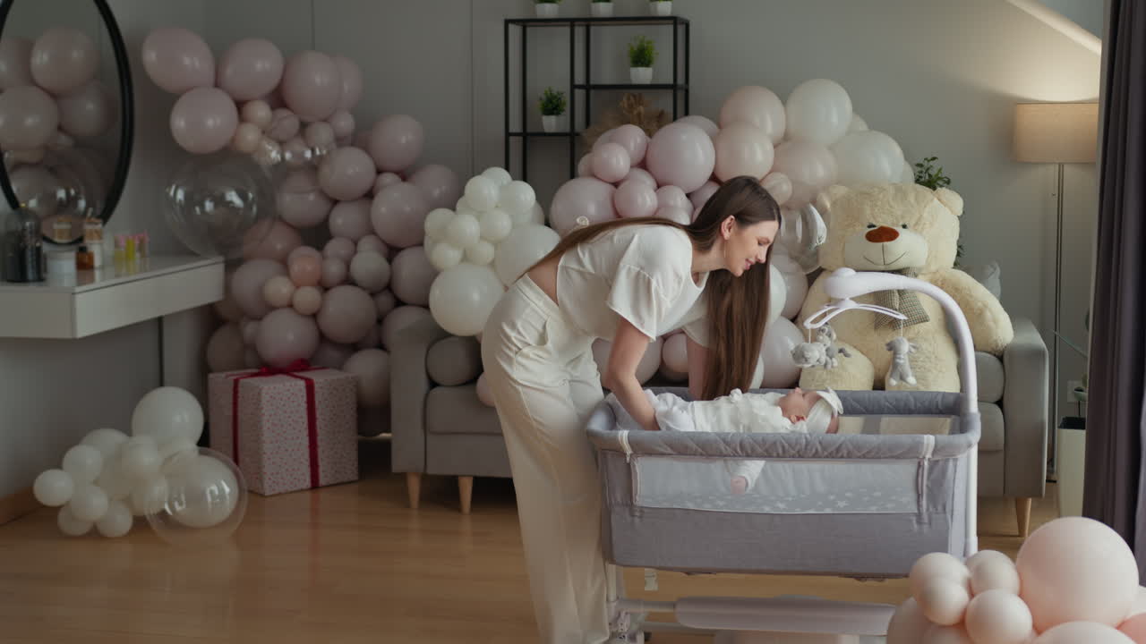 Donna che sistema la culla del bambino tra palloncini pastello e un regalo, creando un'atmosfera festosa nella cameretta