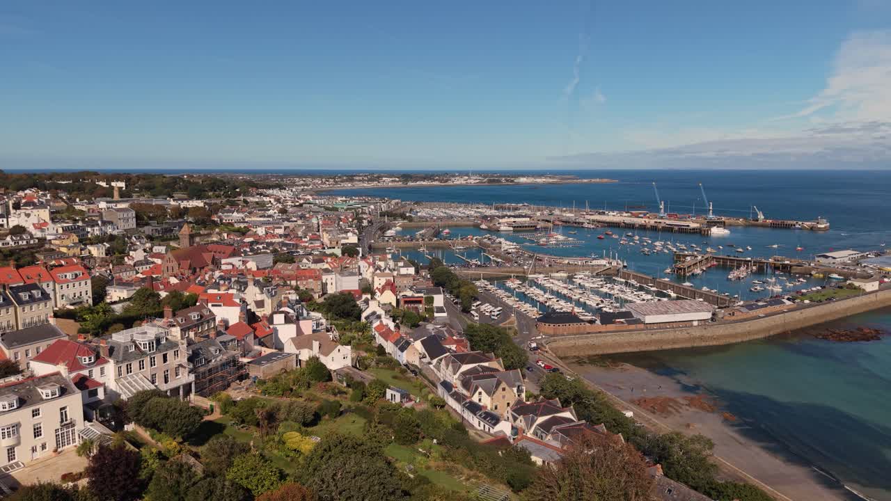 Drone flight across St Peter Port Harbour from Havelet Bay on sunny day with blue sky calm sea and views over town the whole harbour and Belle Greve Bay towards St Sampson