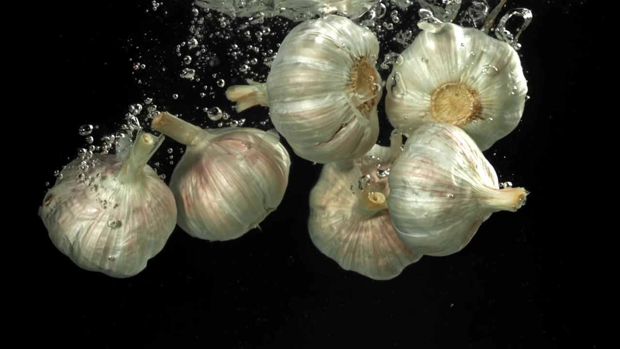 Bulbi d'aglio freschi che cadono nell'acqua al rallentatore